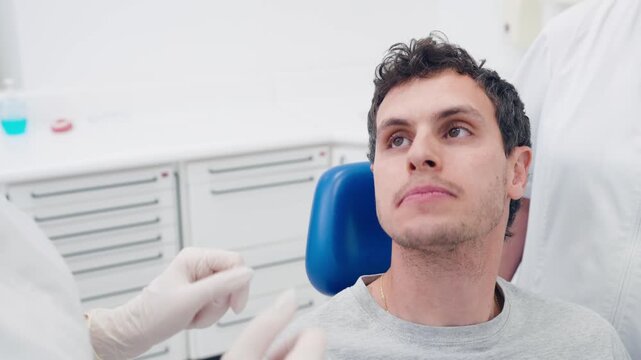 Professional dentist showing a male patient how to properly use dental floss. Oral hygiene and healthcare education during a checkup
