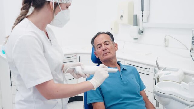 Young female dentist using a 3d intraoral scanner to capture images of a mature male patient's teeth in a modern dental clinic