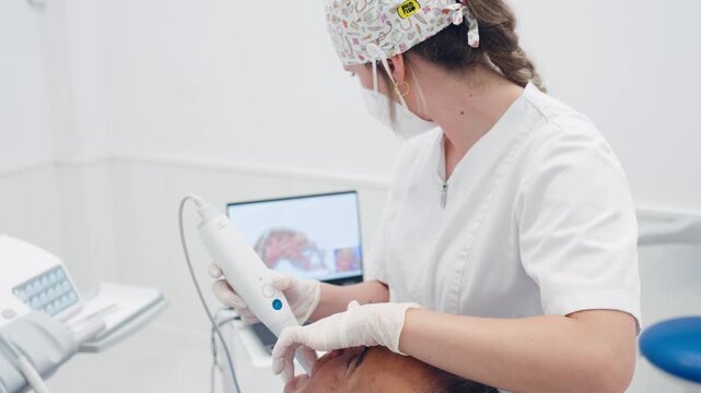 Professional female orthodontist using a digital 3d intraoral scanner for dental impressions, showing the 3d model on a laptop screen
