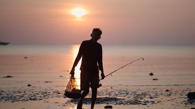 Man holding fishing rod and catch on beach during golden hour sunset