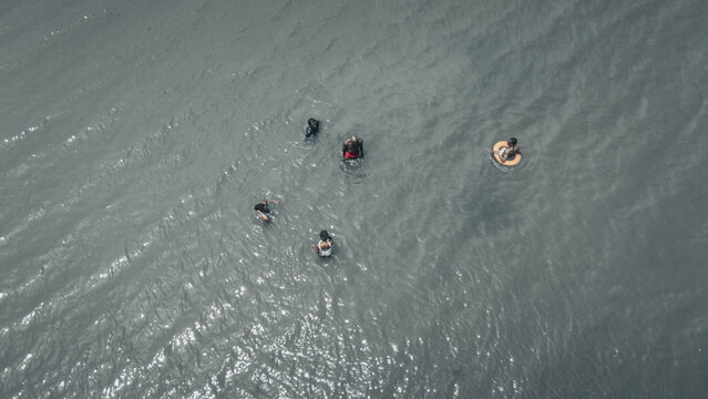 Aerial view of people swimming and floating in the grey rippled waters with one person in an orange lifebuoy Badagry, Lagos, Nigeria.