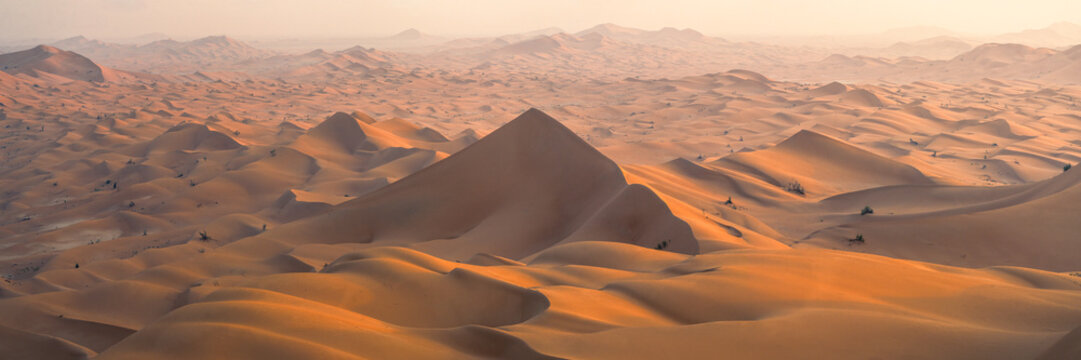Aerial view of the vast sand dunes of the Empty Quarter desert with golden light and a hazy horizon in Ubar, Dhofar Governorate, Oman.