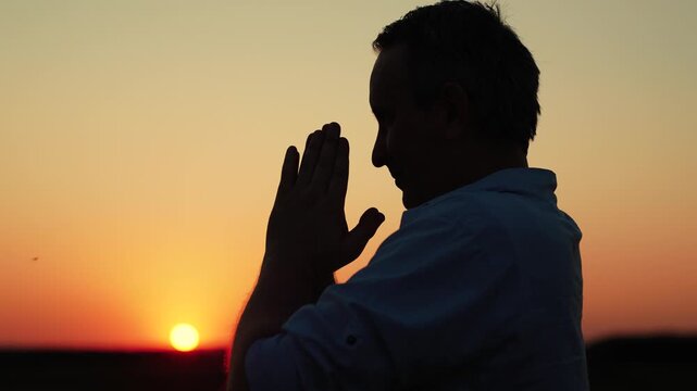 Christian man praying at dawn, close-up. Man confesses. Faith in God. Man prays family children against backdrop sky sun. Relaxation meditation nature. Apologizing. Hope. People religion. Silhouette