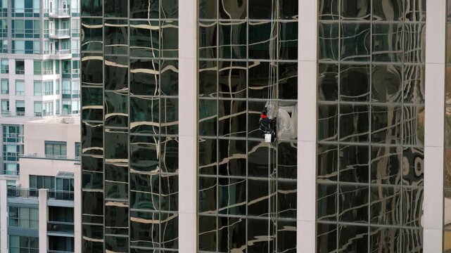 Professional abseiler meticulously descends mirrored building surface near residential areas with controlled precision