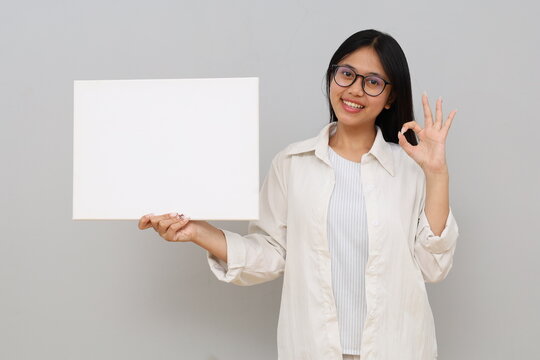 Portrait of a beautiful young Asian woman showing blank white billboard for text and empty space, hand gesture "okay", isolated on white background.