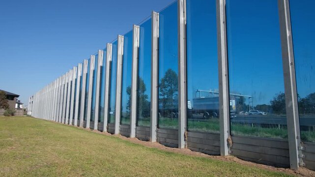 Transparent noise barrier wall alongside a highway in Melbourne, Australia, protecting a residential area from traffic noise with visual permeability. Urban noise mitigation