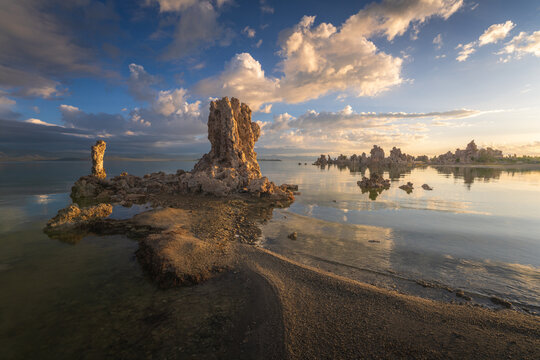 Aerial view of Mono Lake featuring unique tufa towers rising from the calm water under a dramatic sunset sky with golden clouds Mono County, California, United States.