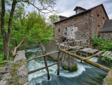 wid angle view to river's flow and old stone water mill with wooden embankment