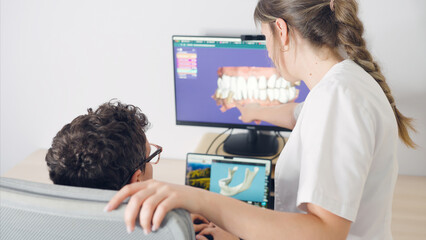 Dentist pointing at a computer screen showing a 3d model of teeth, explaining a treatment plan to a patient © DMegias