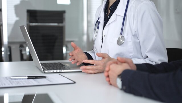 Doctor woman consulting male patient using laptop, discussing health information during medical examination at clinic office. Medicine, healthcare and science concept
