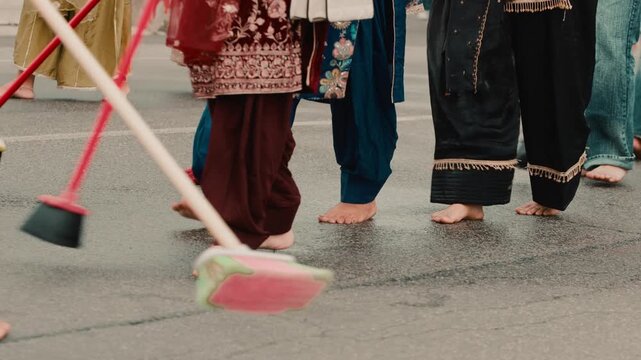 Indian female cleaners sweep the street with brooms during the Sikh procession