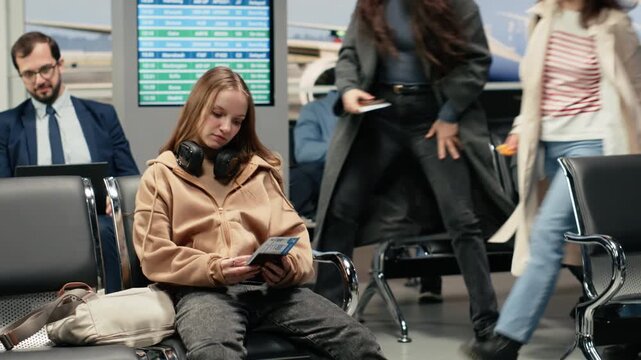 Waiting for airport checkin, airplane ticket and young woman in boarding gate lounge. Doing journey back home, passport document and girl in modern aviation terminal, camera A
