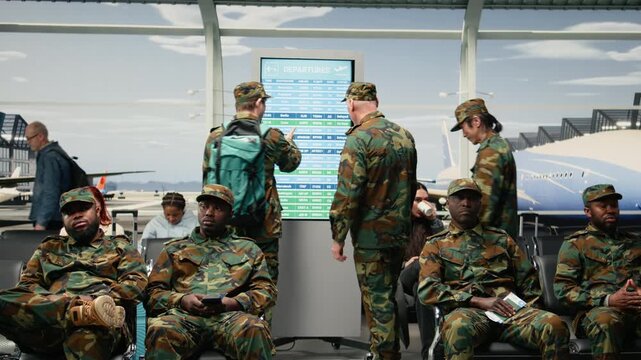 Army men in airport departure lounge looking at flight status display timetable. Military squad reading electronic departure board schedule, waiting for plane arrival, camera A