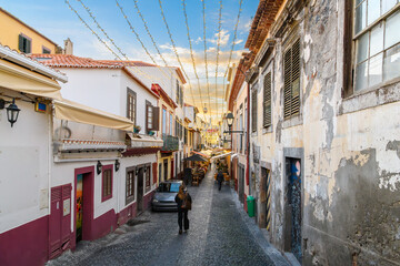 A cable car gondola to the town of Monte passes over the famous Rua de Santa Maria narrow street of sidewalk cafes, shops and colorful painted doors in Funchal, Portugal, Madeira Island. © Kirk Fisher