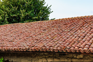 Fototapeta premium Traditional clay roof tiles on rustic stone building with lush greenery