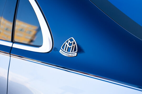 Luxury car Mercedes Maybach badge featuring the emblem of a limited edition model on a sleek blue vehicle exterior with reflections of surrounding architecture visible