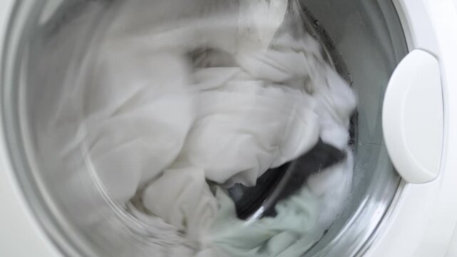 Washing machine filled with white and light green laundry items in a spinning cycle, showcasing the movement and water action inside the transparent drum