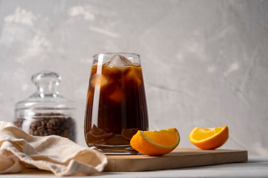 Coffee with orange juice bumble in a tall glass with ice on a light background with coffee beans, fruits and morning shadows
