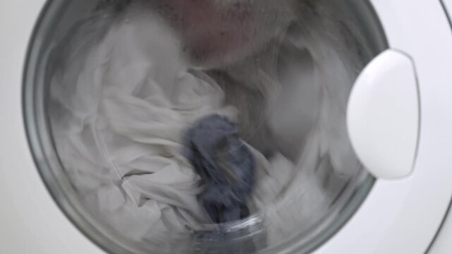 Washing machine in action with white laundry spinning inside the drum, showcasing the continuous cycle of the home laundry process in a modern appliance setting
