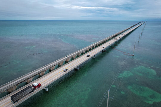 Aerial view of The Overseas Highway stretching across turquoise waters with vehicles driving under a cloudy sky in Key Largo, Florida, United States.