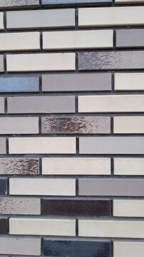 Modern brick wall texture with narrow decorative clinker bricks in grey, beige, and brown tones. Seamless horizontal pattern of contemporary facade material for architectural design