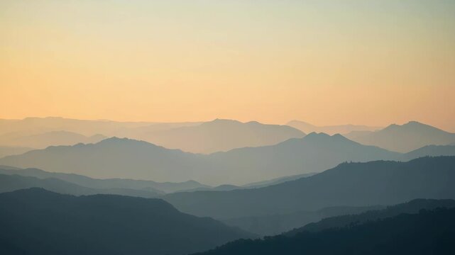 Misty layered mountain range at sunrise with soft pastel sky and serene haze mist layers