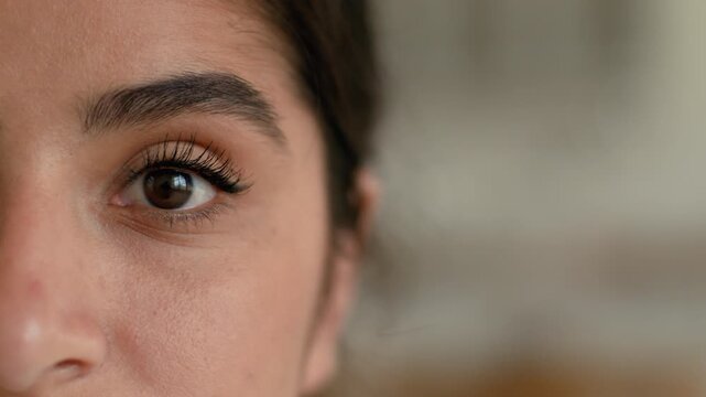 Extreme close up of calm Indian Arabian woman at home half face cropped view female girl looking at camera dark eye healthy young eyesight clinic laser correction ophthalmology health medicine indoors