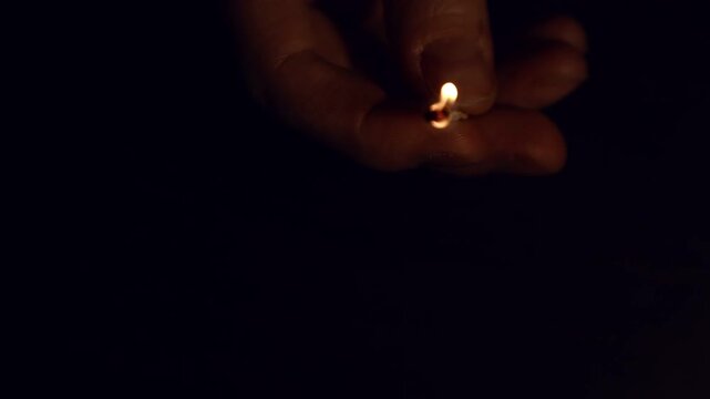 A woman strikes a match with her fingers against a matchbox. Burning match in her hand isolated on black background with empty copy space. Closeup