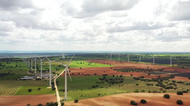 Aerial views reveal stunning wind farms stretching across vibrant fields and rolling hills. Nature and technology harmonize beneath clouds, showcasing eco-friendly energy.