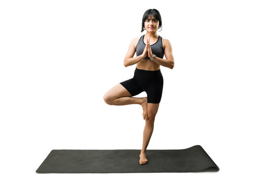 Full length view of a woman practicing yoga tree pose, balancing on one leg, meditating for wellness and health