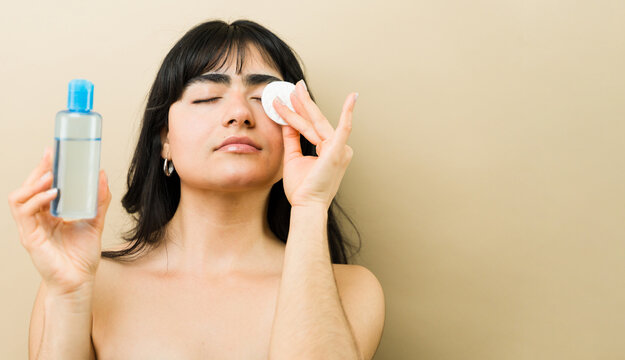Woman removing makeup with micellar water and cotton pad, showing daily facial cleansing routine and skin care