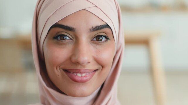 Excited surprised Indian Muslim woman shocked looking at camera in pink hijab at home smiling saying wow reacting good news winning Arabian female amazed happy Islamic girl positive emotion indoors