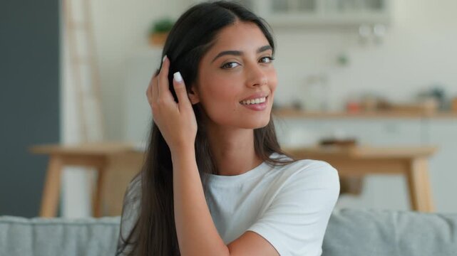 Happy smiling Indian Arabian woman combing dark healthy shiny hair at home indoor glad female girl relaxing self care beauty routine brushing hairstyle comb hairbrush haircare shampoo conditioner mask