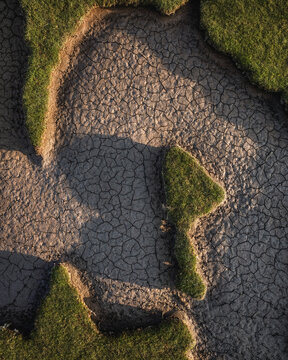 Aerial view of the intricate patterns of cracked dry earth bordered by vibrant green grass at Portmarnock Beach County Dublin, Ireland.