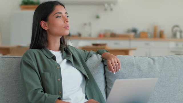 Pensive Indian woman using laptop computer thinking typing freelancer at home student Arabian female ethnic girl businesswoman browsing online shopping booking food delivery order internet app indoors