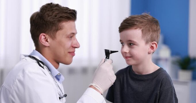 Hearing test. Doctor examining boy's ear with otoscope in clinic. Camera spinning