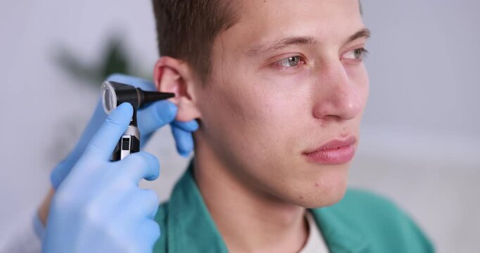 Hearing test. Doctor examining man's ear with otoscope in clinic, closeup. Camera moving