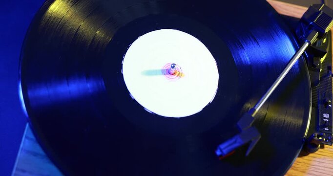 Modern turntable with vinyl record on table in color lights, closeup