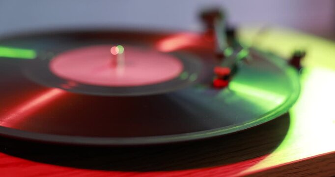 Modern turntable with vinyl record on table in color lights, closeup