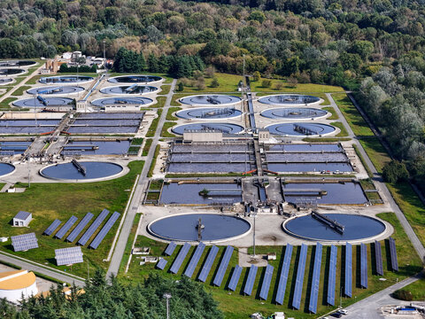 Aerial view of the Impianto depurazione water treatment plant featuring circular clarifiers and solar panels surrounded by lush forest in Castiglione Torinese, Piedmont, Italy.