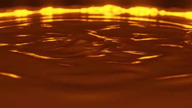 Golden liquid surface with expanding ripples and glowing orange light reflections.