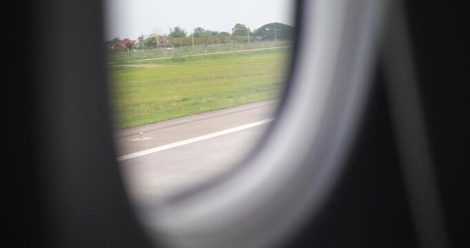 Cinematic close-up view through an airplane window during taxi on the runway, blurred green landscape and airport ground background, travel and aviation concept