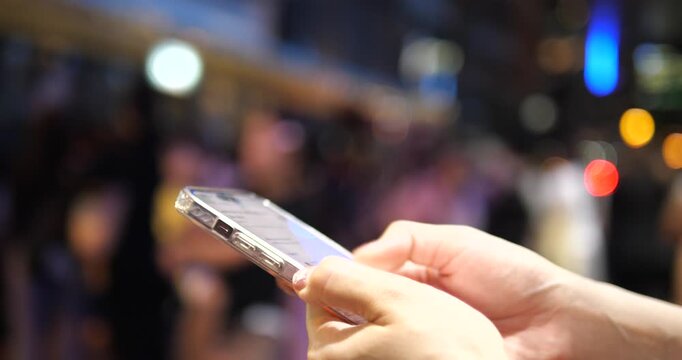 Cinematic close-up of hands using a smartphone on a city street at night, beautiful colorful bokeh background and urban lifestyle concept