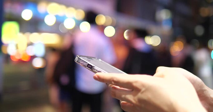 Cinematic close-up of hands using a smartphone on a city street at night, beautiful colorful bokeh background and urban lifestyle concept