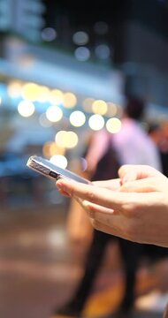 Cinematic close-up of hands using a smartphone on a city street at night, beautiful colorful bokeh background and urban lifestyle concept