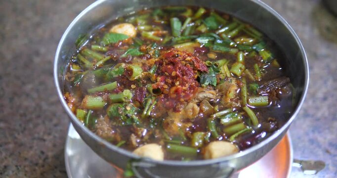 Cinematic close-up of Thai spicy braised beef soup (Gao Lao) in a hot pot, rich Tom Yum Nam Tok broth with chili paste and meatballs