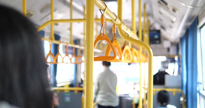 Cinematic close-up of yellow handrail grips inside a public bus, blurred interior with passengers and urban transportation concept