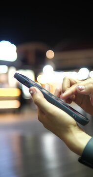 Cinematic close-up of hands using a smartphone on a city street at night, beautiful colorful bokeh background and urban lifestyle concept