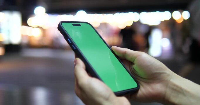 Cinematic close-up of a hand holding a smartphone with green screen chroma key, beautiful colorful city bokeh background at night