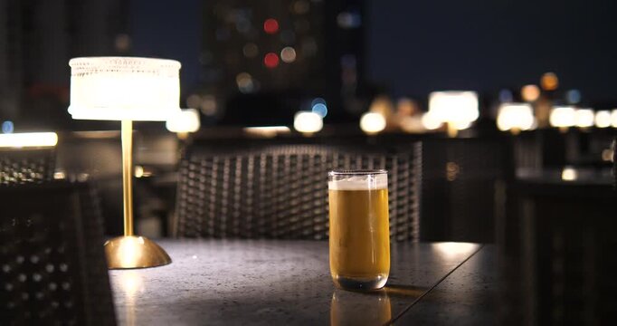 Cinematic close-up of a glass of cold beer on a table at night, luxury cruise or rooftop bar atmosphere with elegant lamp and bokeh background